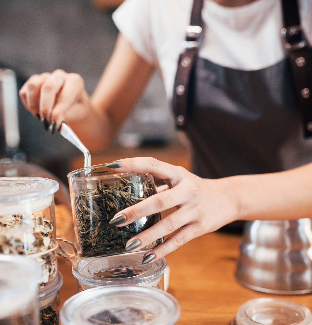 Person preparing tea with a glass container on a wooden surface