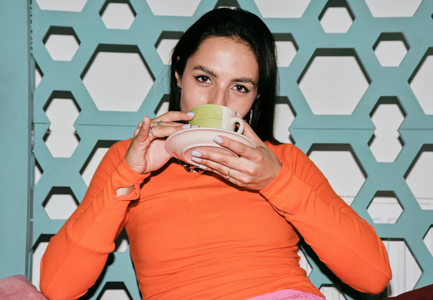 Woman in an orange shirt holding a pink tea cup 