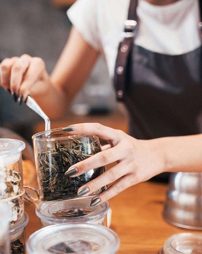 Person holding a glass of green tea leaves with a blurred background
