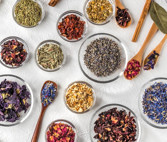 Assorted dried herbs and spices in small glass bowls on a light surface.